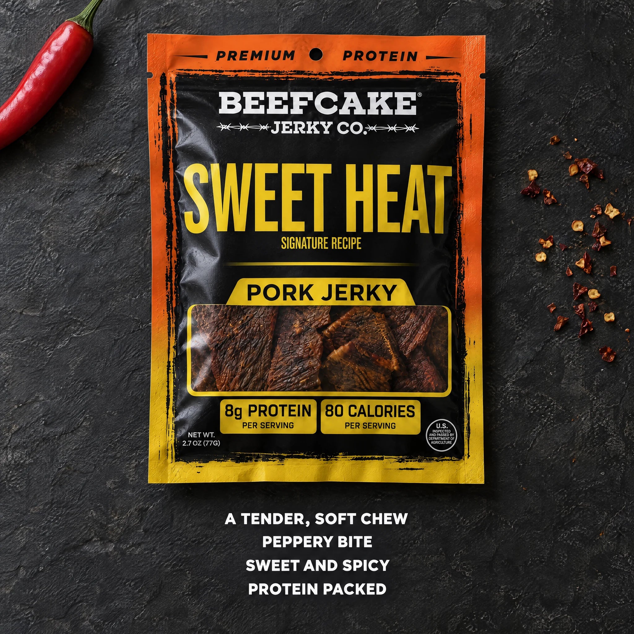 BeefCake Sweet Heat pork jerky with a red chili and chili flakes on a dark slate surface.