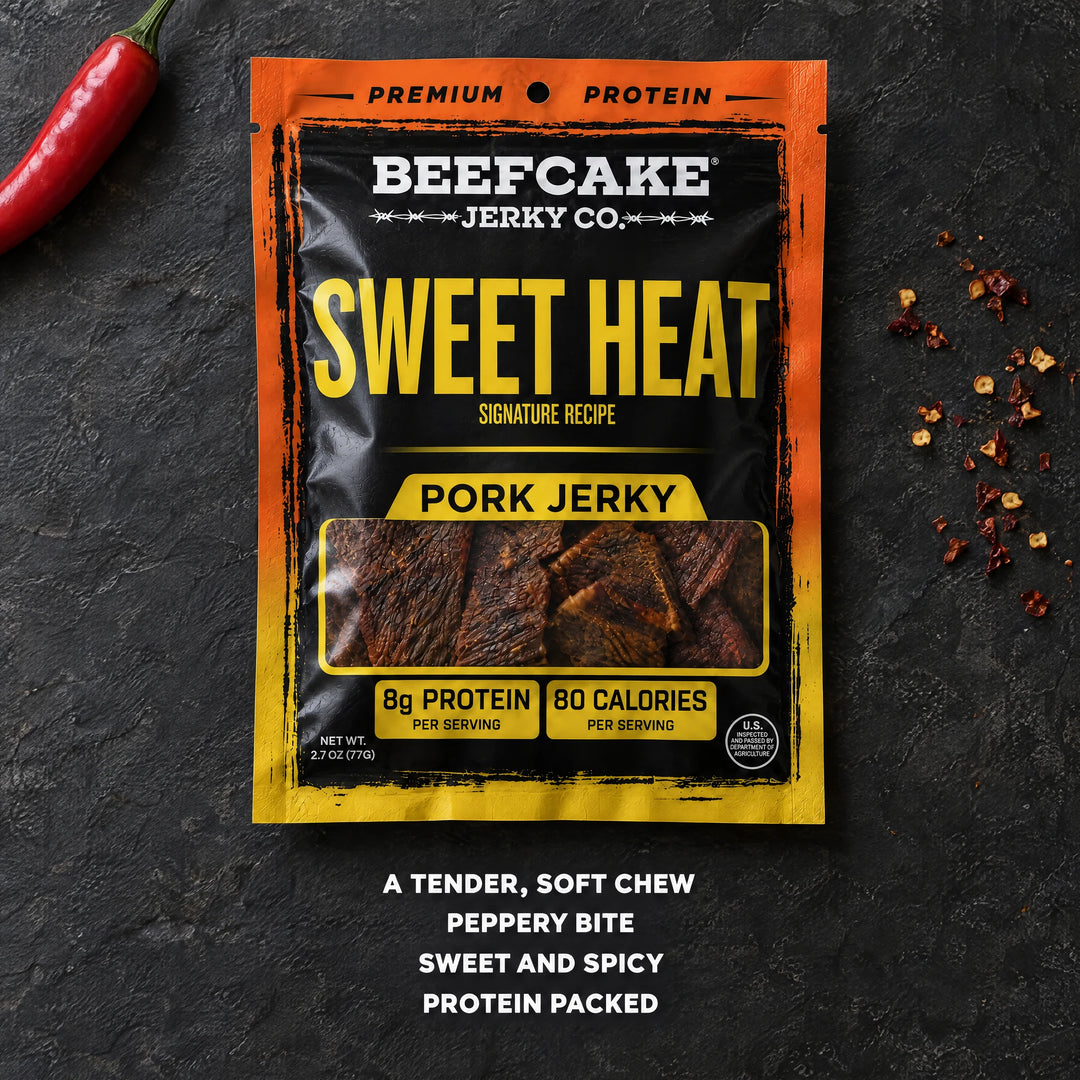 BeefCake Sweet Heat pork jerky with a red chili and chili flakes on a dark slate surface.