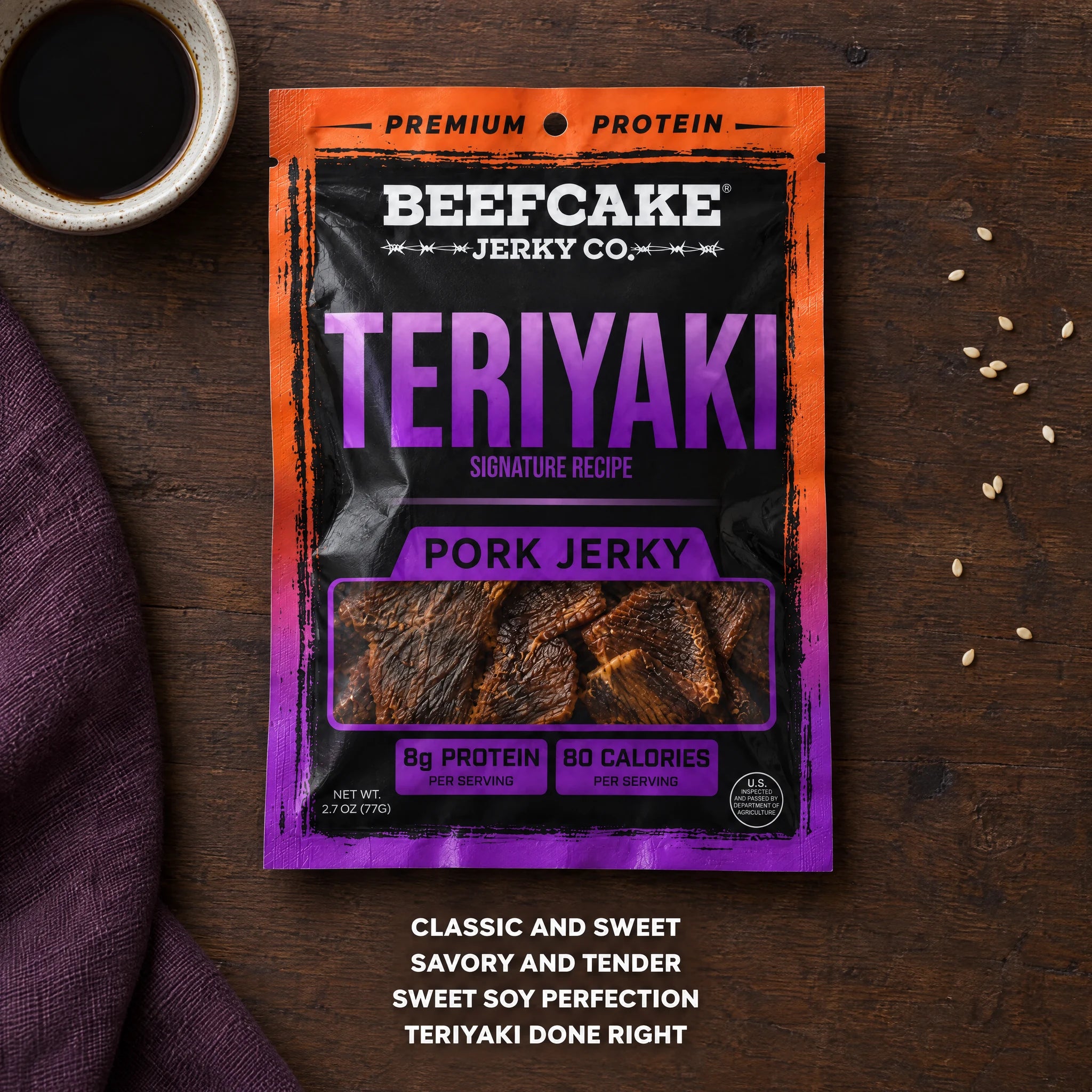 BeefCake Teriyaki pork jerky with soy sauce and sesame seeds on a wooden table.
